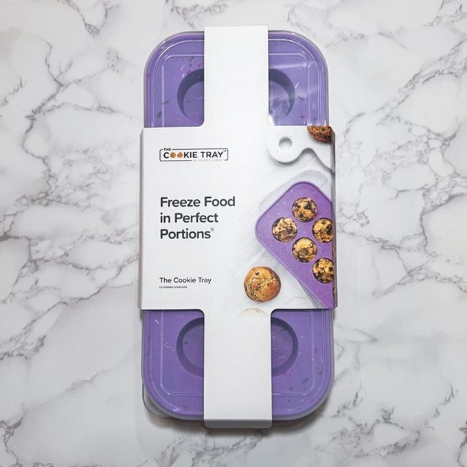 A purple rectangular freezer tray with a white label that reads "Freeze Food in Perfect Portions" and shows images of cookies, lying on a white marble surface.
