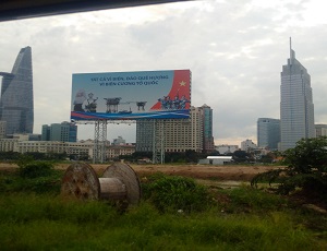 A wooden roll empty of coil sits in grassland, rapidly to be replaced by some of the largest developmental projects and buildings Vietnam has ever seen in its history. The billboard above talks about defending Vietnam's sea borders.